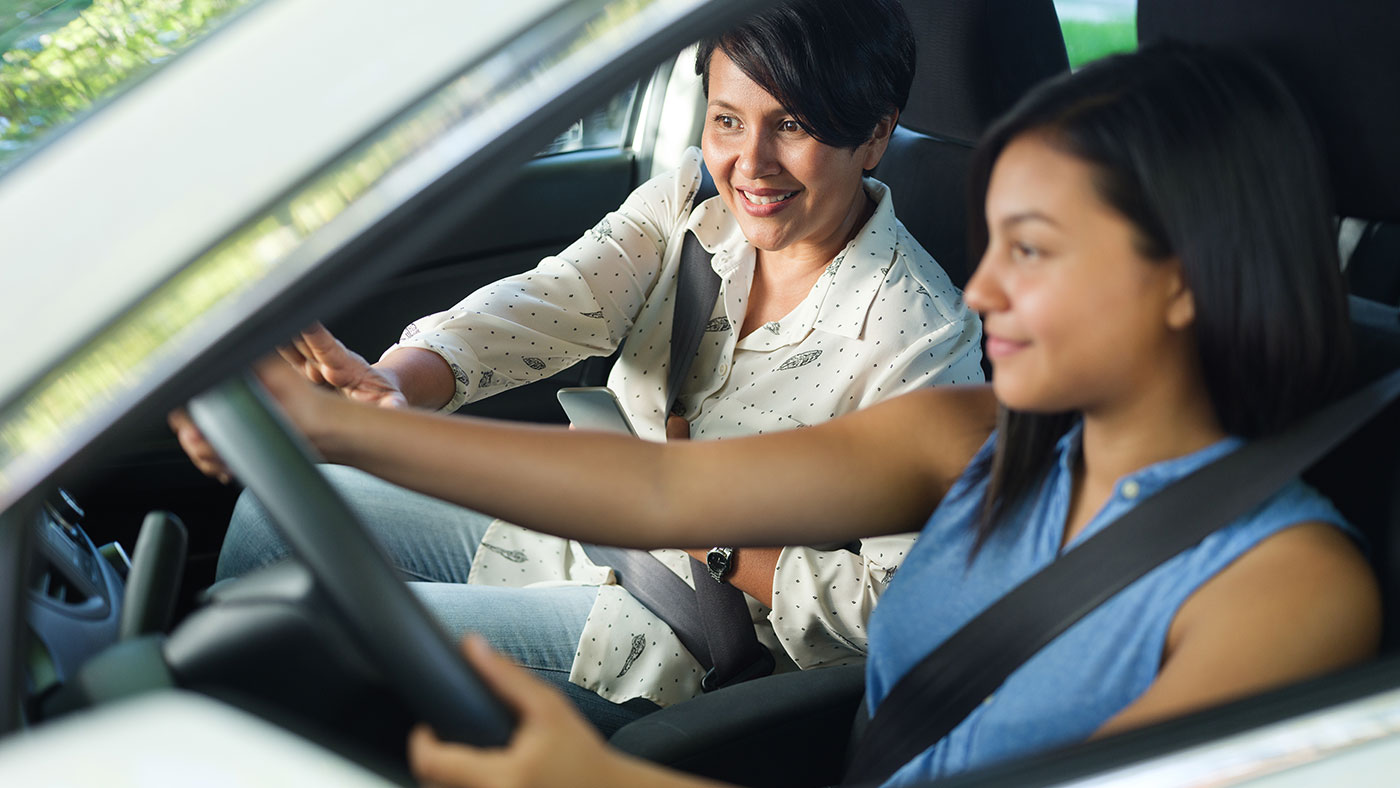 Two women seated in a car with one driving and the other in passenger seat, both wearing seatbelts.